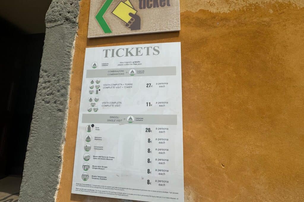 Ticket pricing board on the wall at the Leaning Tower of Pisa showing entry fees for tower and monuments
