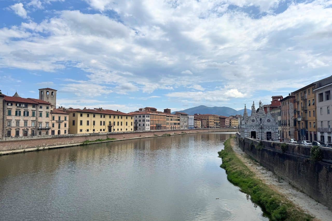 Peaceful view of the Arno River with colorful buildings lining the riverbanks and 5 star hotels in Pisa Italy in the distance. 