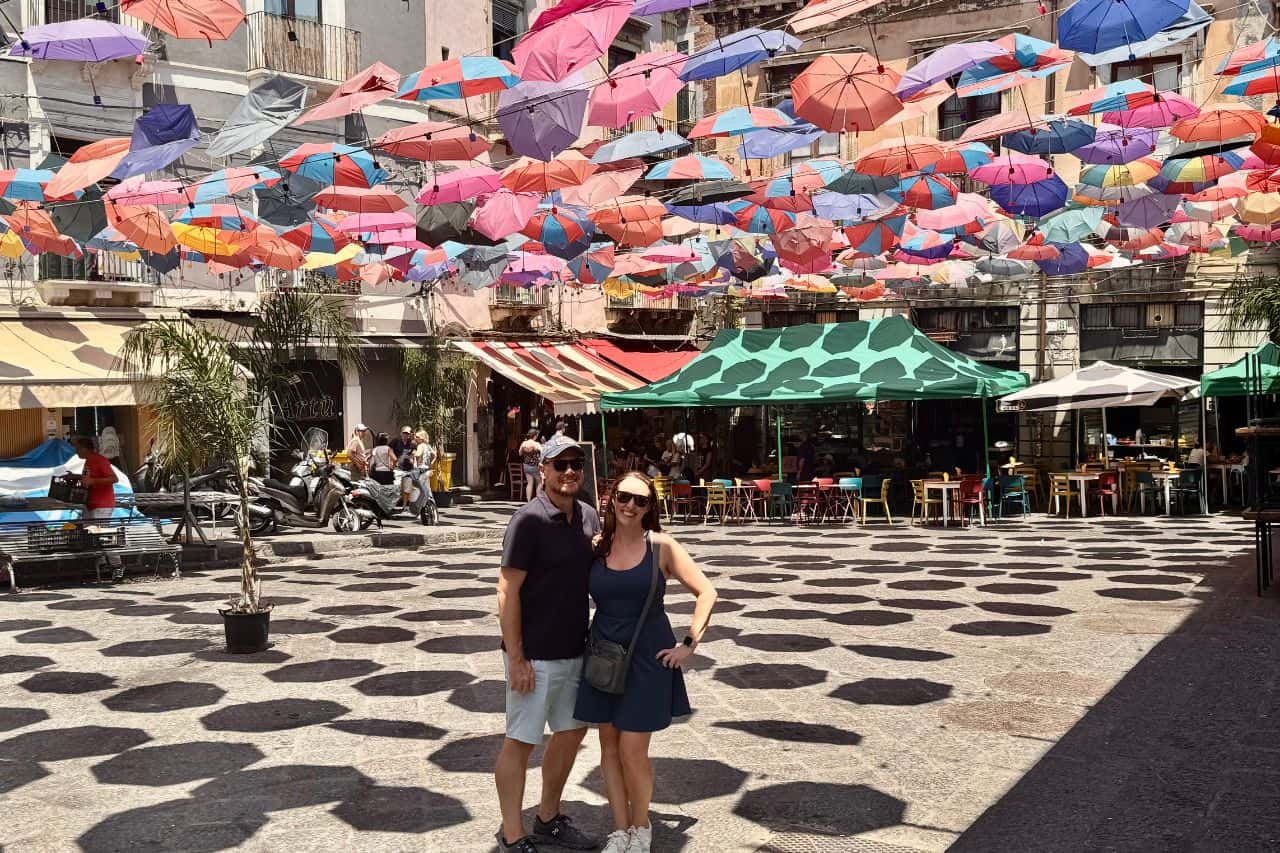 Two tourists standing under the popular rainbow umbrella street in Catania