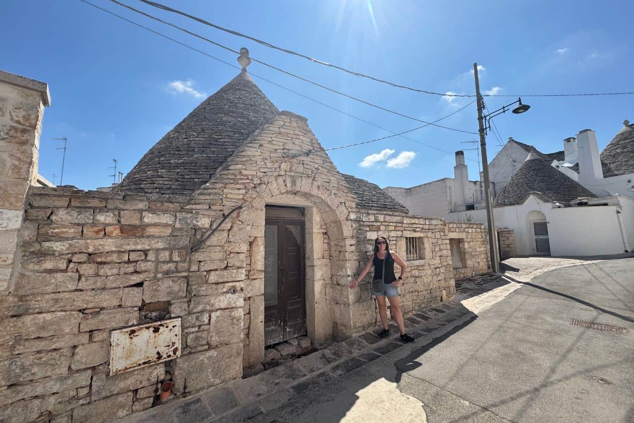 Row of traditional white Trulli houses with cone-shaped roofs lining a cobblestone street in Alberobello, one of the easy day trips from Bari 